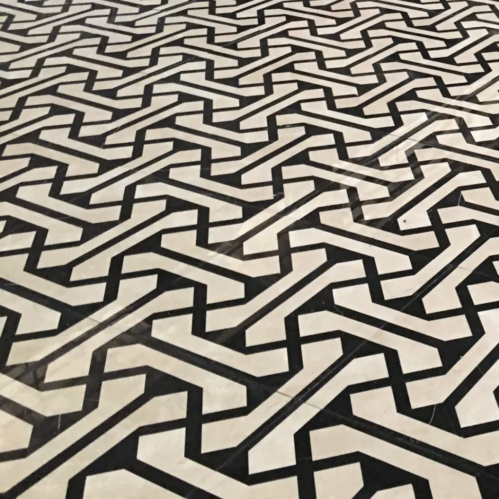 A main high-angle photograph of a bespoke modern interlocking geometric Arabesque lattice waterjet medallion flooring pattern, crafted from high-contrast Calacatta White and Nero Marquina black marble for luxury interior design.